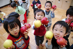 写真：カメラに向かってりんごを見せる園児たち