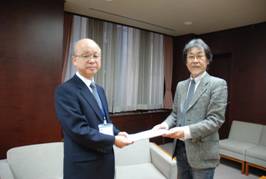 新宿区協働事業提案制度審査会長から区長(代理:副区長)へ報告書を提出する様子<左から永木副区長、久塚審査会長>